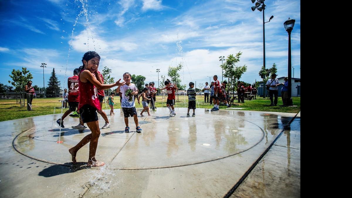 
Children run through the new splash pad at McNamara Park in Merced on June 30. 
