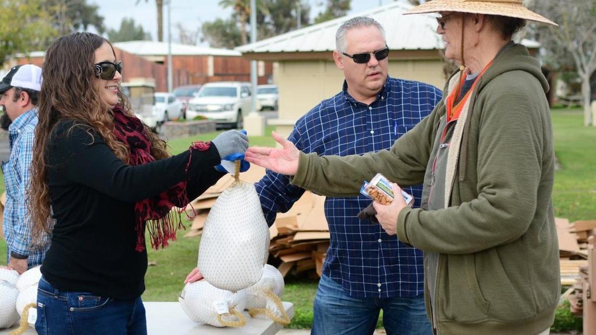 Lindsey Butts, left, hands out a turkey during Hostetler Ranches’ and Joseph Farms’ turkey, almond and cheese giveaway on Monday in Los Banos.