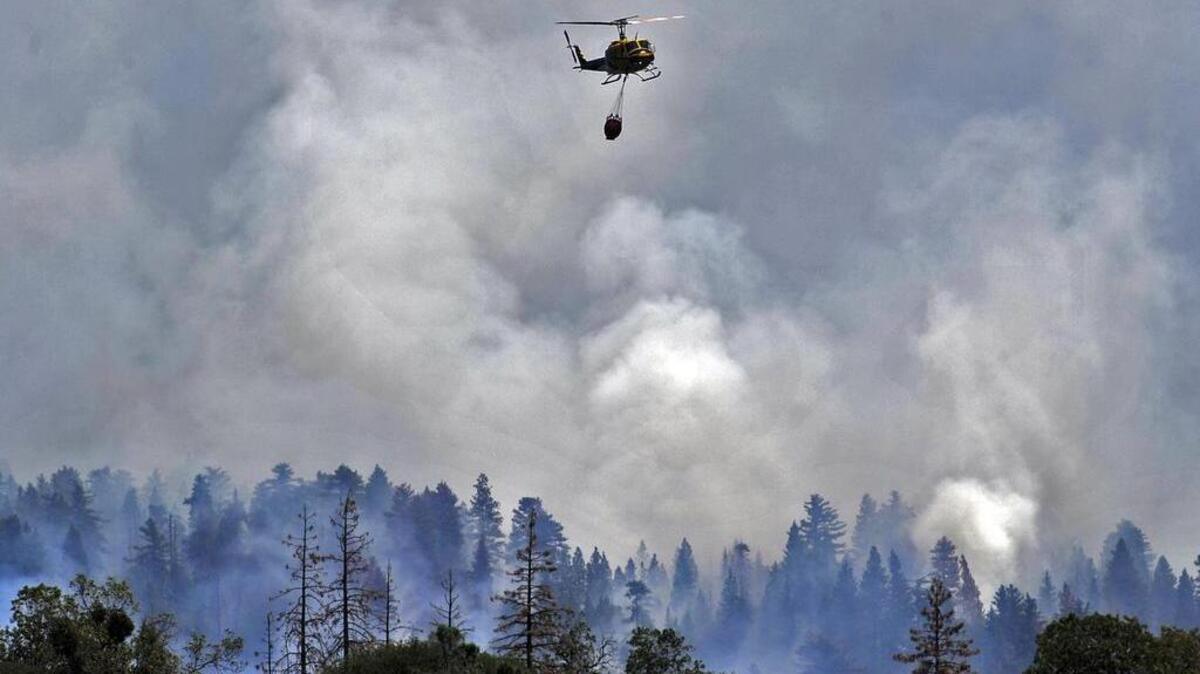 
A helicopter flies away from a burning ridge after dropping water on the Willow fire near Bass Lake on Monday.
