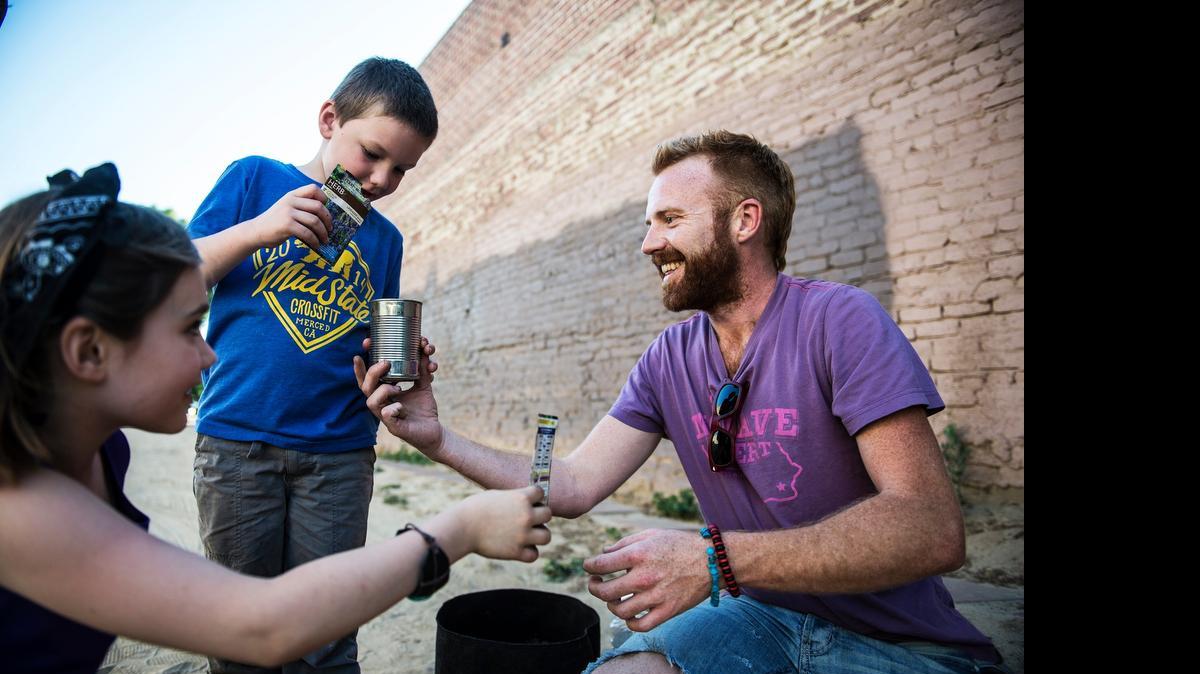 
Eric Jacobs, 32, of Merced, assists Ava Martin, 7, and Bodie Martin, 5, both of Merced, in planting seeds in a tin can during April’s Merced Art Hop.
