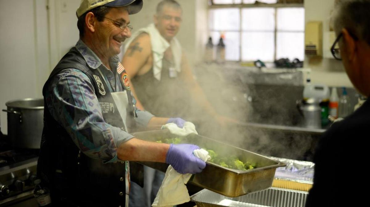 David Mansfield, vice president of the Prayer Warriors Motorcycle Ministry, transfers steaming hot broccoli into a pan at the American Legion Hall during the annual Thanksgiving meal. Hundreds of people ate and picked through donated clothes.