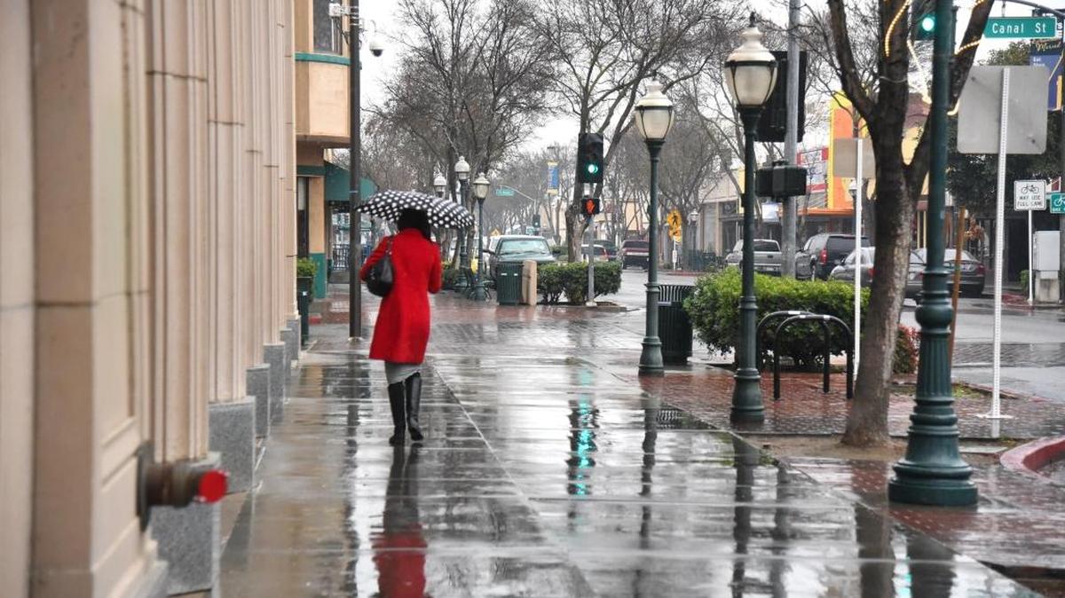 A woman using an umbrella walks in the rain down Main Street in Merced in January.