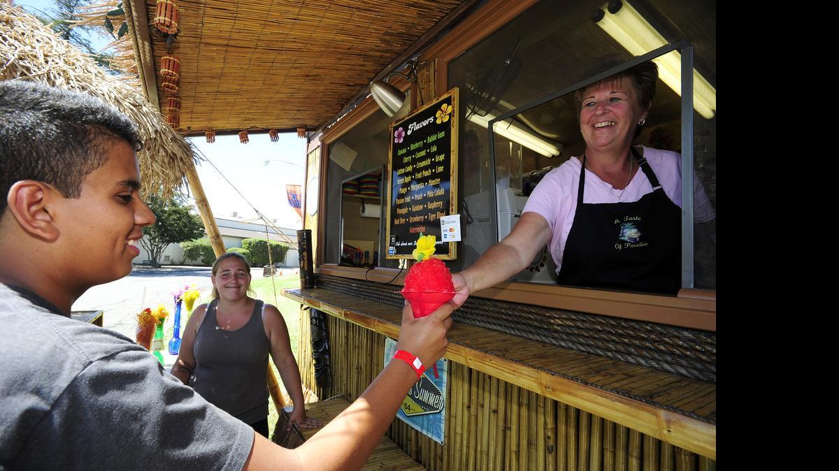 
Kim Sanders of Taste of Paradise Hawaiian Shave Ice serves up a cup of shaved ice, at the fairgrounds on Monday  in Merced.
