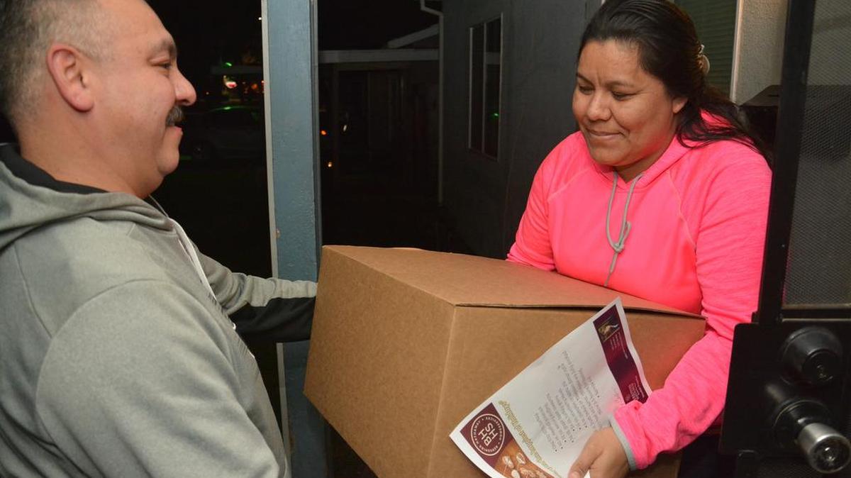 Andrew Borrego gives a Los Banos resident a free ready-to-eat family meal Tuesday. Henry Miller Elementary staff and supporters teamed with local Berkshire Hathaway Realtors to carol and provide free meals to needy families in Los Banos.