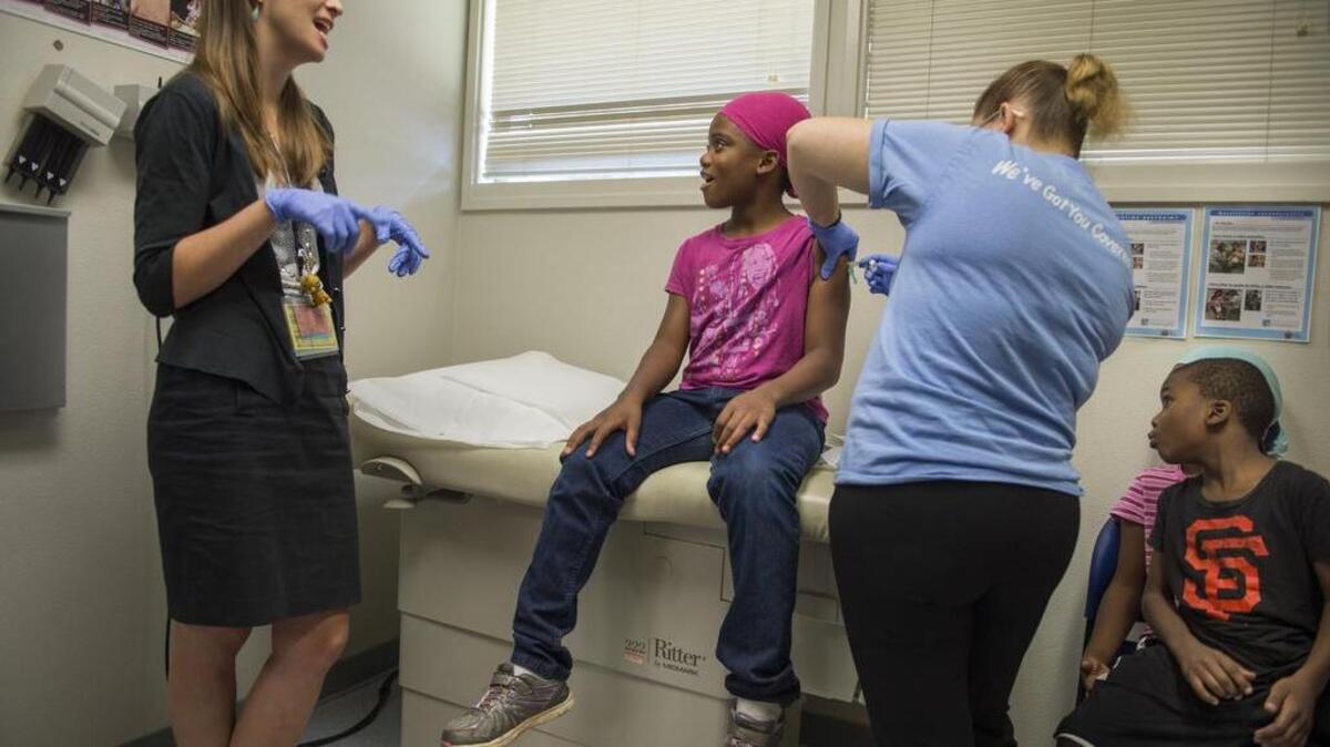 Dr. Emy Daniel, a resident pediatrician with UC Davis, left, talks with Lamaria Harris, 9, to keep her focus away from getting a booster shot as her little brother, Neeko Harris, 5, right, gets a good look at the injection administered by Marciela Magallon, a medical assistant with Well Space Health, on Aug. 4, 2016, at the Oak Park Health Center.