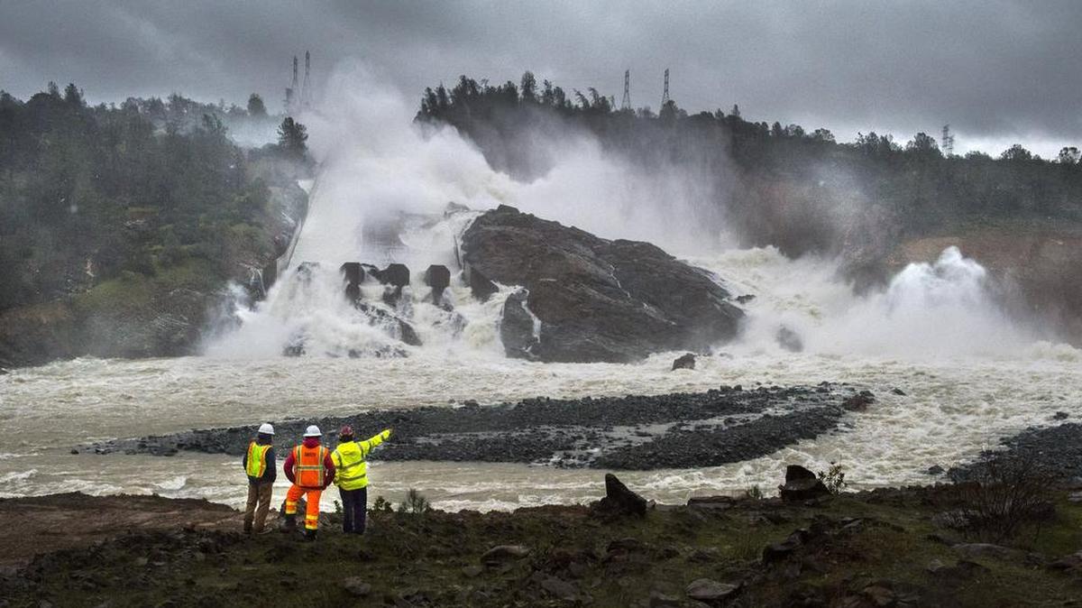 A state firefighter, right, talks to workers on the Oroville Dam project in front of the dam’s crumbling main spillway on Feb. 20, 2017. On Monday, it was shut down so that debris could be removed from the bottom of the spillway, allowing the dam’s electrical turbines to be restarted.
