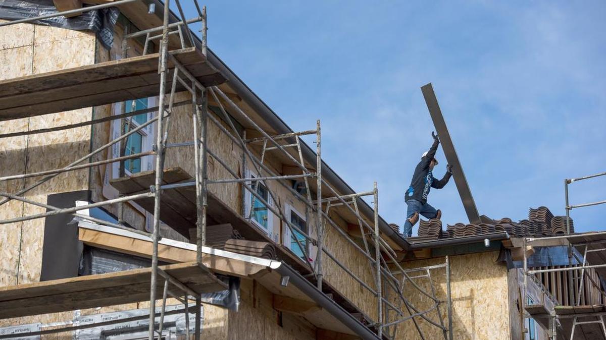 A contractor moves roofing material on a home under construction in San Ramon in January. While California is now building about 100,000 units of new housing each year, it falls short of demand and doesn’t reduce a million-unit shortage.