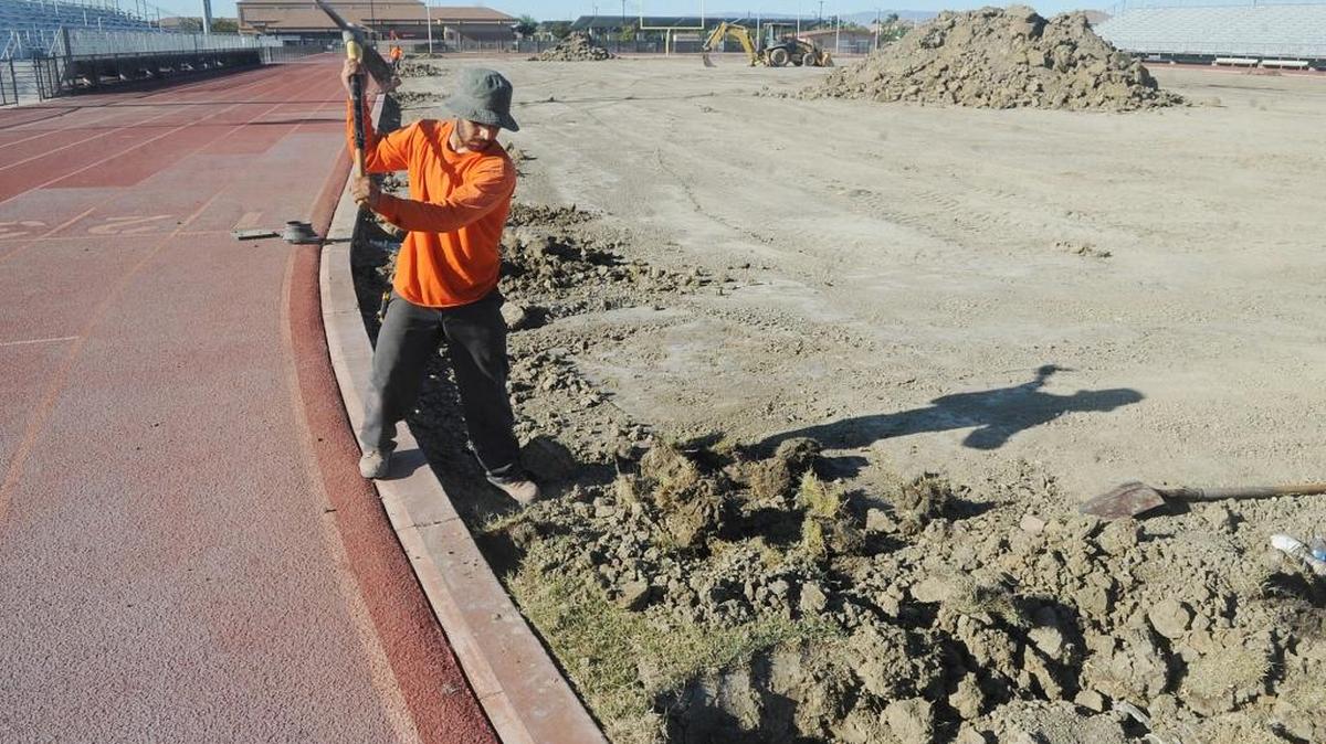 Robert Servin of Gilroy, who works for Goodland Landscape Construction of Tracy, uses a pick hoe to remove the last of the dead sod from the football field at Veterans Stadium at Pacheco High in Los Banos on Wednesday in preparation for the installation of artificial turf.